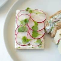 A closeup of an open-faced sandwich with herb butter, sliced radish and micro greens