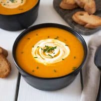 Roasted Carrot Ginger Soup in a black bowl with spoon and crusty bread
