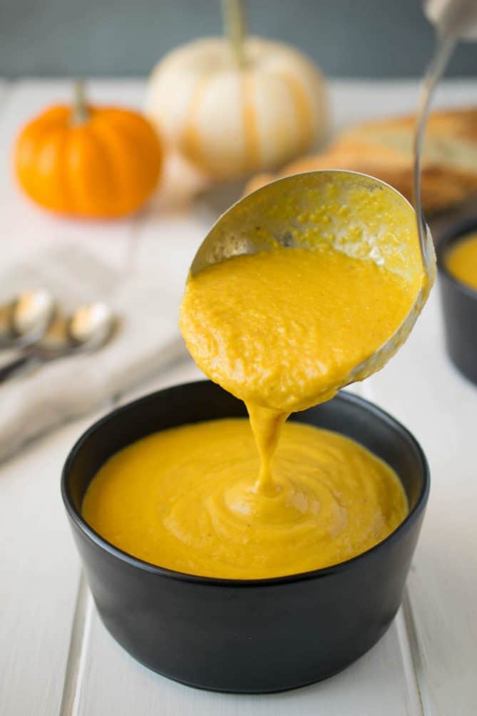 Using a ladle to pour pumpkin vegetable soup into a black bowl