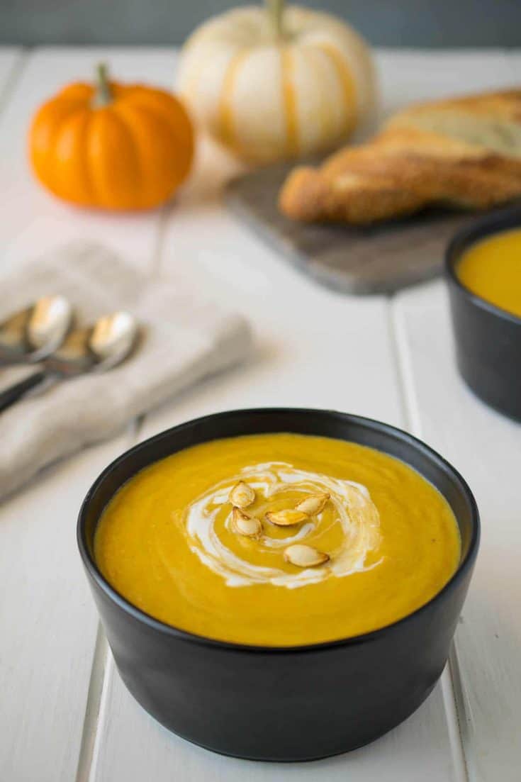 A round black bowl filled with roasted pumpkin and root vegetable soup garnished with a swirl of sour cream and roasted pumpkin seeds