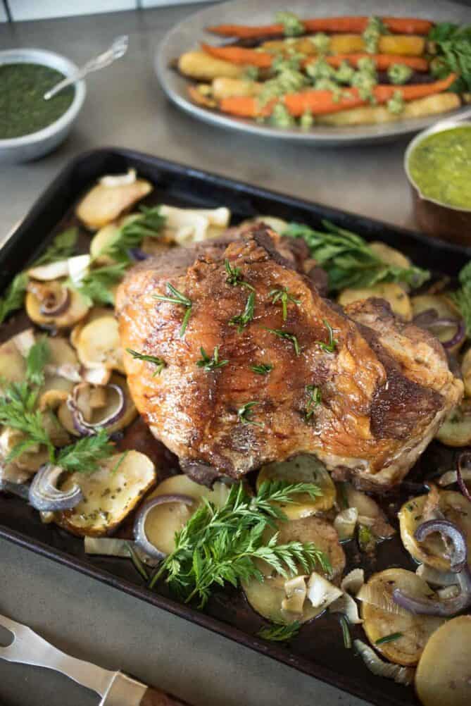 A pan of sliced potatoes, fennel and onion in a roasting pan topped with roast lamb