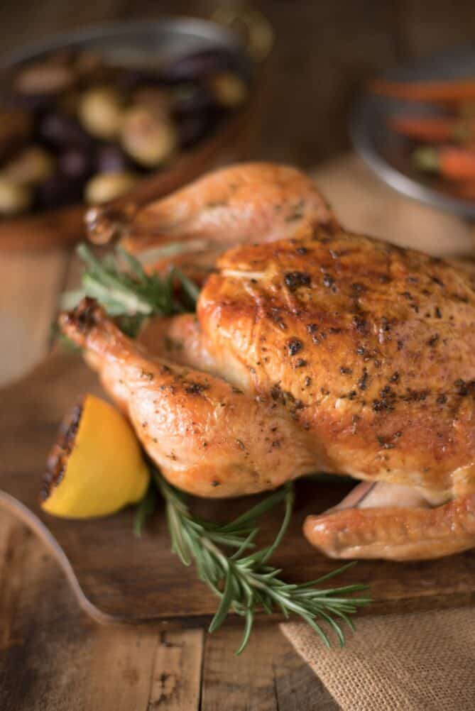 A closeup of a roasted chicken leg seasoned with fresh rosemary