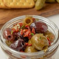A jar filled with black and green olives mixed with sun-dried tomatoes and fresh rosemary