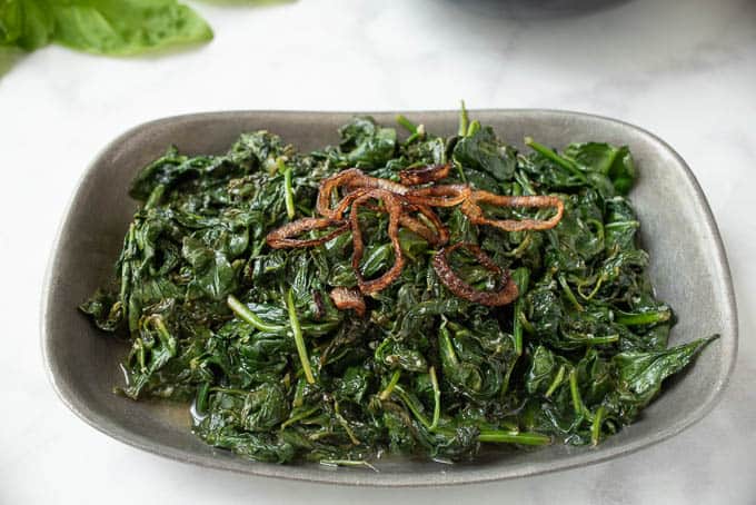 Sauteed spinach with crispy shallots in a grey bowl