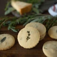 Herb and parmesan shortbread crackers displayed on a board with fresh herbs