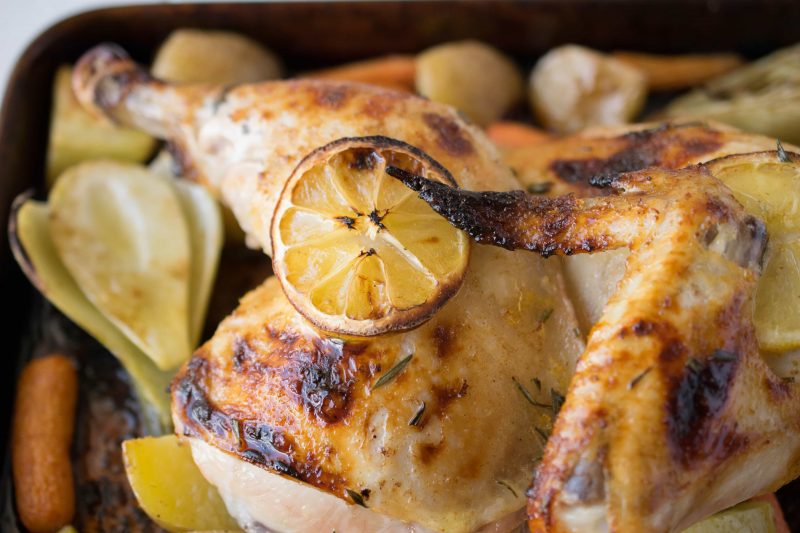 A closeup of half a roasted chicken with a slice of lemon