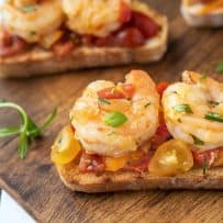 Grilled bread slices topped with shrimp and cherry tomatoes
