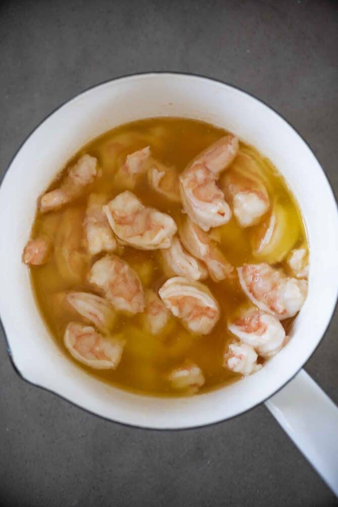A white enamel pan of melted butter cooking shrimp