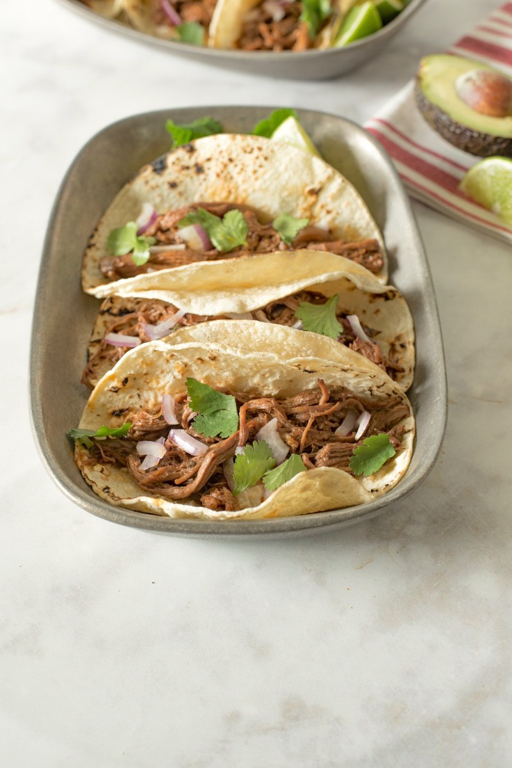 Slow cooker barbacoa tacos. Beef roast is slowly cooked in a homemade guajillo chile pepper sauce until it is fall apart and shredded, served simply in soft tortillas with red onion and cilantro.