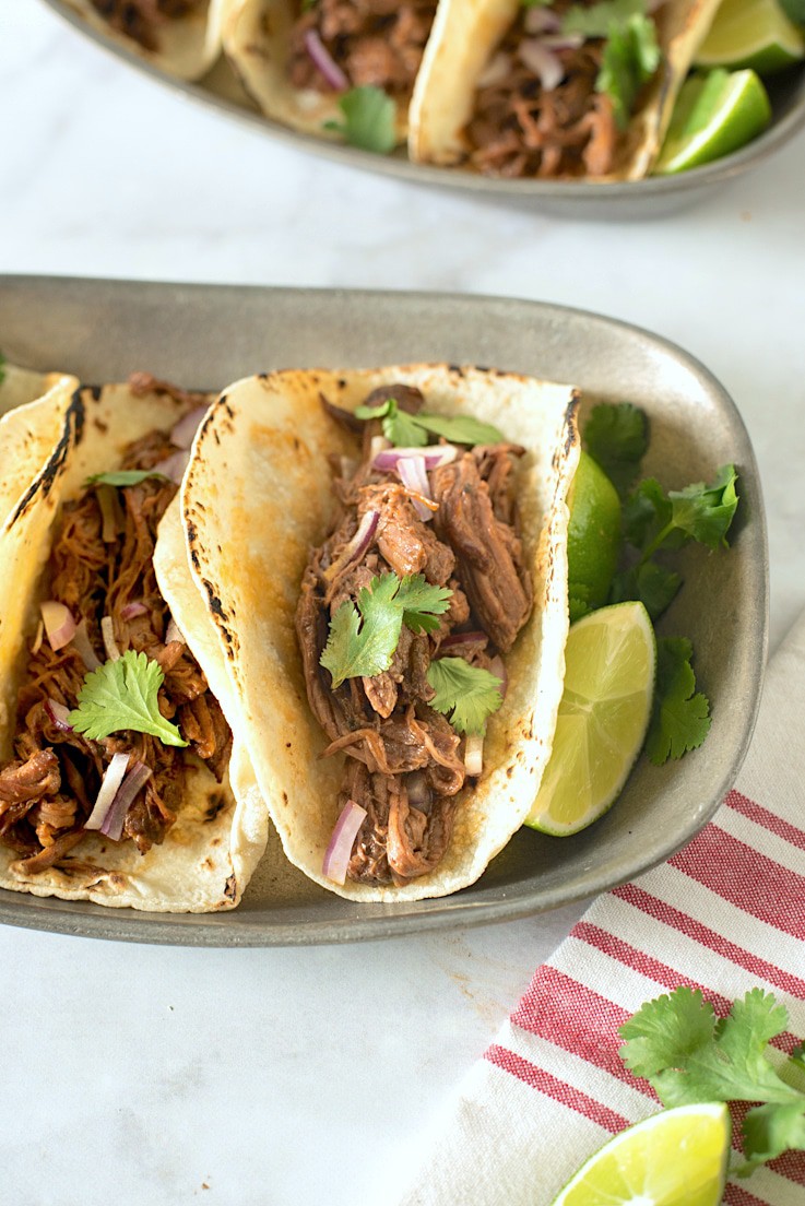 Slow cooker barbacoa tacos. Beef roast is slowly cooked in a homemade guajillo chile pepper sauce until it is fall apart and shredded, served simply in soft tortillas with red onion and cilantro.