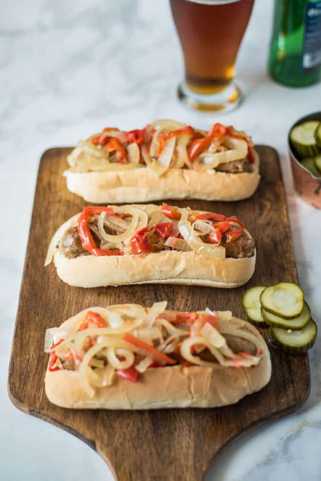 3 bratwurst sandwiches on a board with pickles