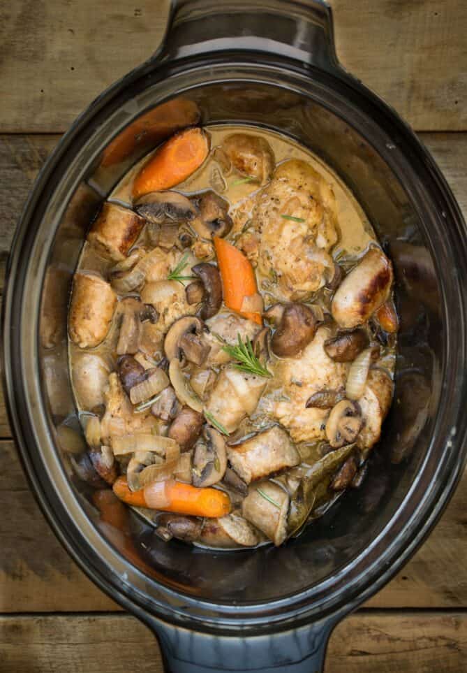 A slow cooker filled with chicken, sausage, mushrooms and carrots