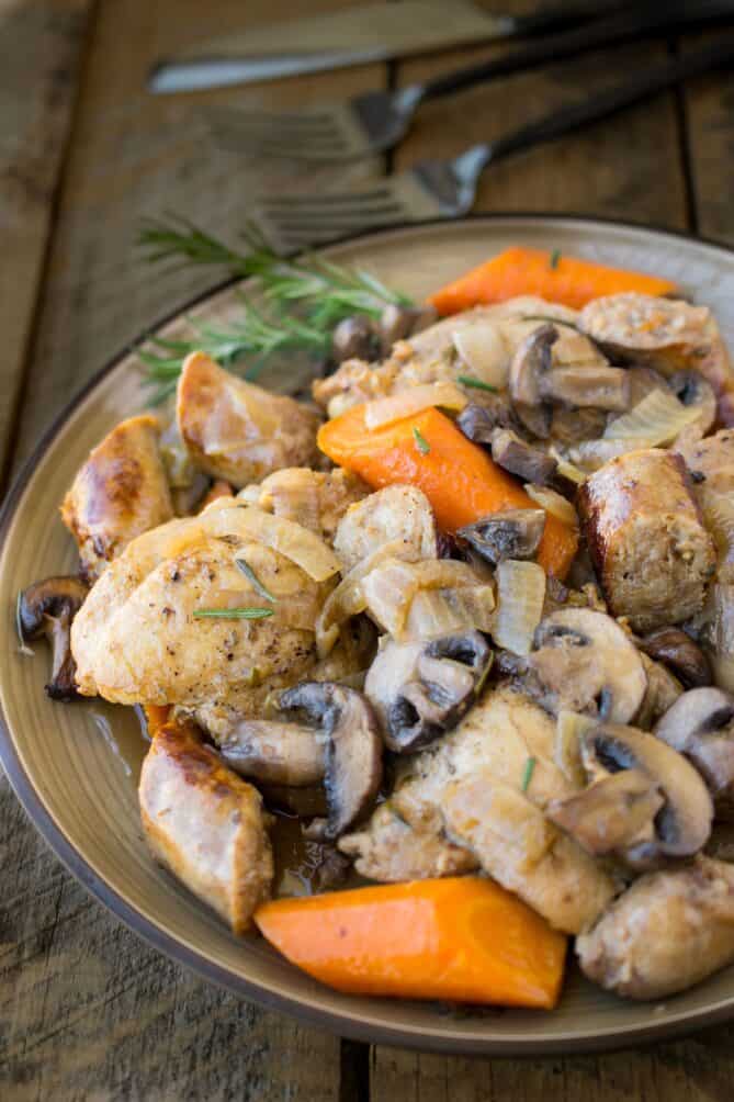 A close up of a plate of chicken, sausage, mushrooms and carrots