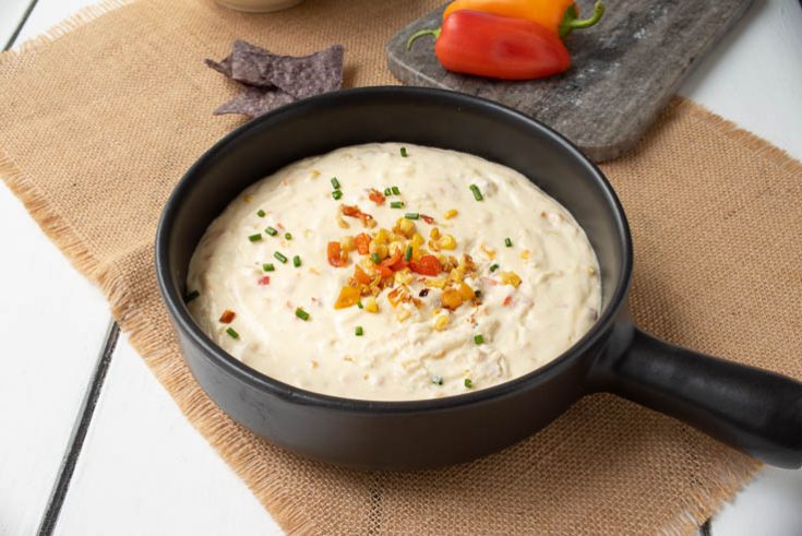 The dip in a black bowl garnished with corn, peppers and green chives