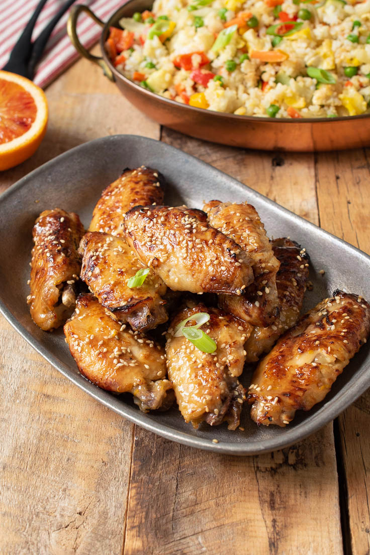 Orange chicken wings brown and crispy topped with sesame seeds with a side of fried rice
