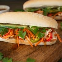 Shredded chicken, carrot slaw, cilantro and cucumber spilling out of a banh mi sandwich