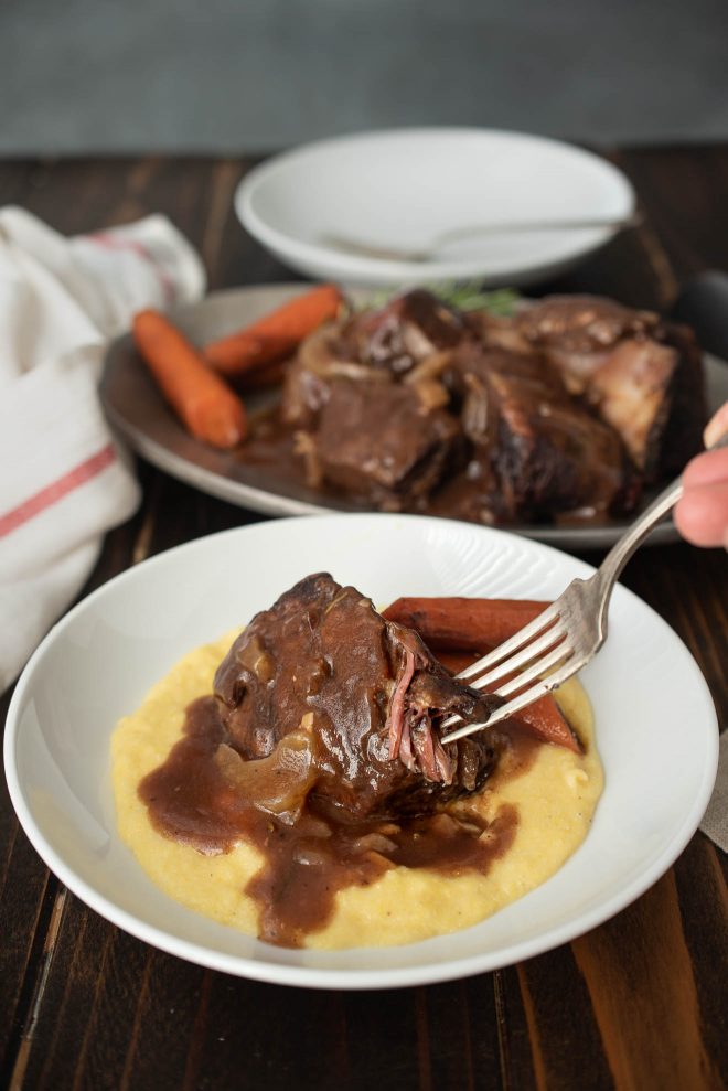 Beef short ribs on polenta with carrots on a white plate