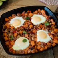 Sweet potatoes, sausage and bacon cooked in a cast iron skillet topped with 4 sunny side up eggs