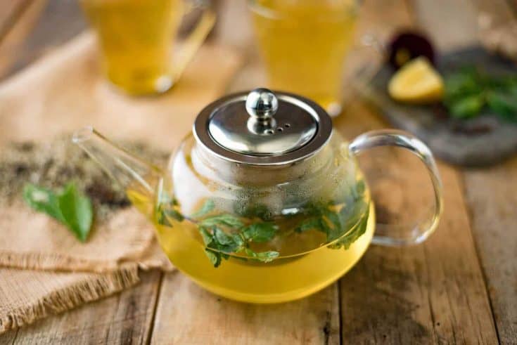 Fresh herbs floating in herbal tea in a clear teapot
