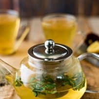 A glass teapot of herbal tea with fresh herbs