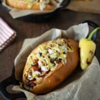 A bacon wrapped hot dog in a bolillo bun with toppings