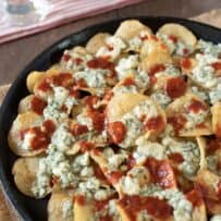 A closeup of potato chips with melted blue cheese and hot sauce
