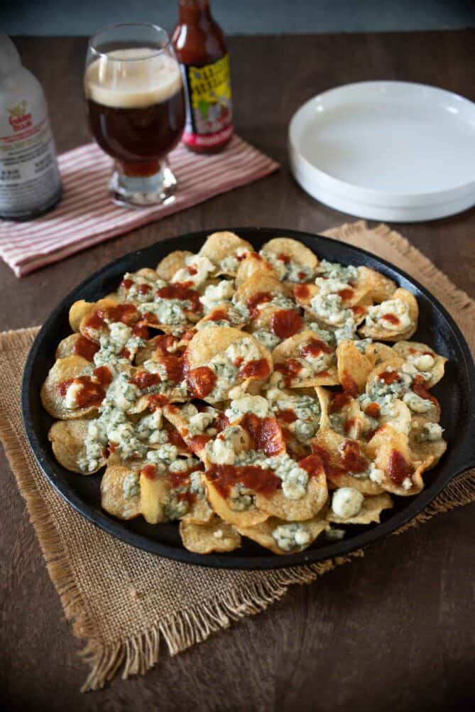 A cast iron platter covered with potato chips topped with melted blue cheese and jalape&ntilde;o spicy sauce