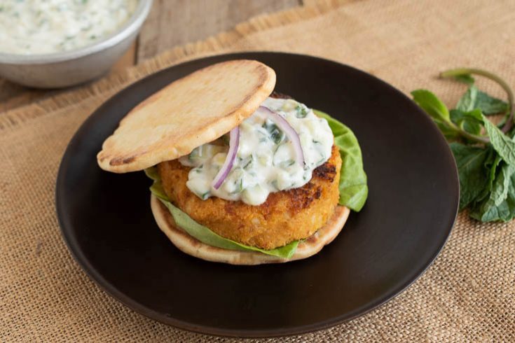 A deliciously browned veggie burger on a naan bun with lettuce topped with raita