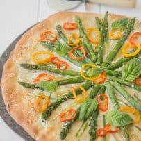 A closeup of asparagus, colorful peppers and basil are the colorful toppings on the pizza