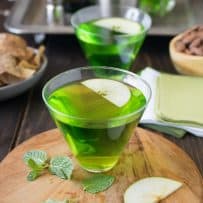 A vibrant green cocktail garnished with sliced apple