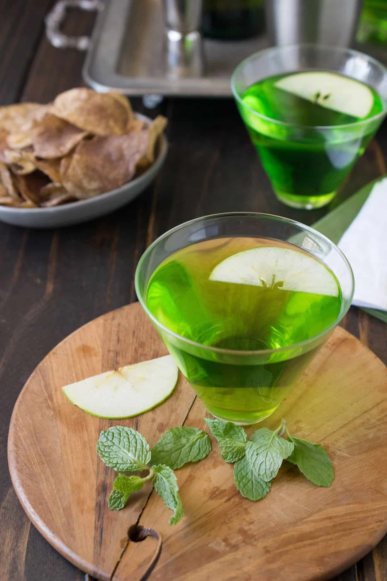 2 glasses of St Patrck's Day green Dublin cocktail on a board with fresh mint and apple slices