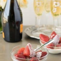 A side view of a glass bowl of whole strawberries with fresh cream with a spoon