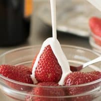 A closeup of a red whole strawberry being smothered in fresh cream