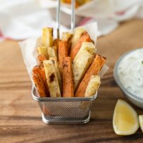 Orange and white baked fries in a basket with yogurt sauce and lemons