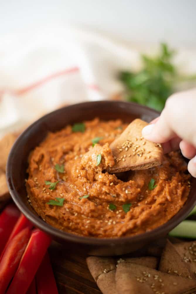 A wooden bowl filled with sun-dried tomato hummus with a toasted pita chip