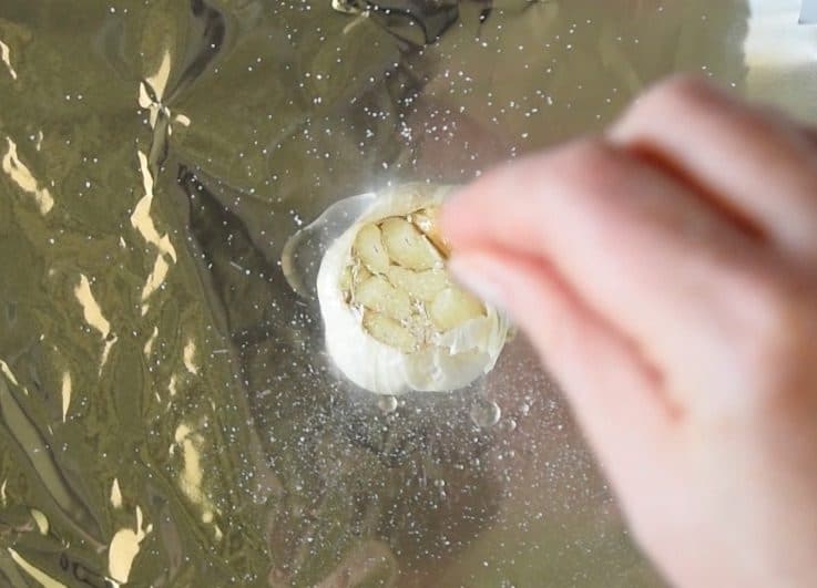 A head of garlic on foil drizzled with oil and salt