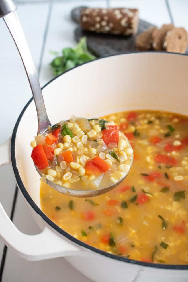 A ladle full of corn and vegetable soup