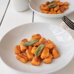 2 white bowls of sweet potato gnocchi garnished with crispy sage