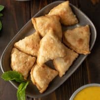 A platter of sweet potato samosas viewed from above with fresh mint