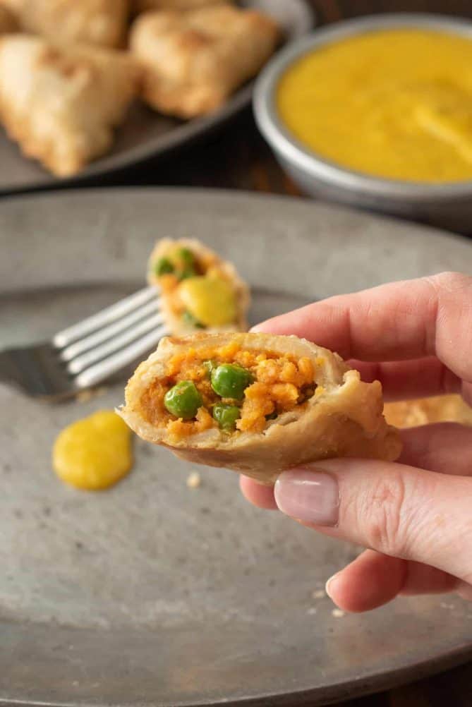 A samosa cut open showing sweet potato and pea filling inside