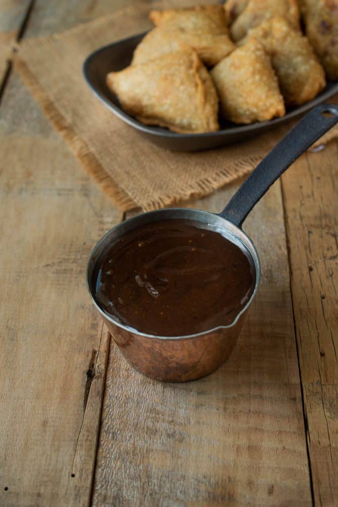 A small copper pan filled with dark brown tamarind date chutney
