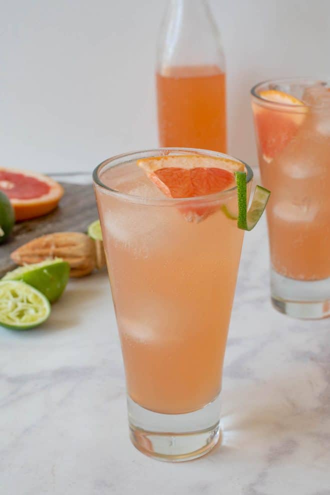 A tall glass of tequila Paloma garnished with a wedge of fresh grapefruit and lime rind