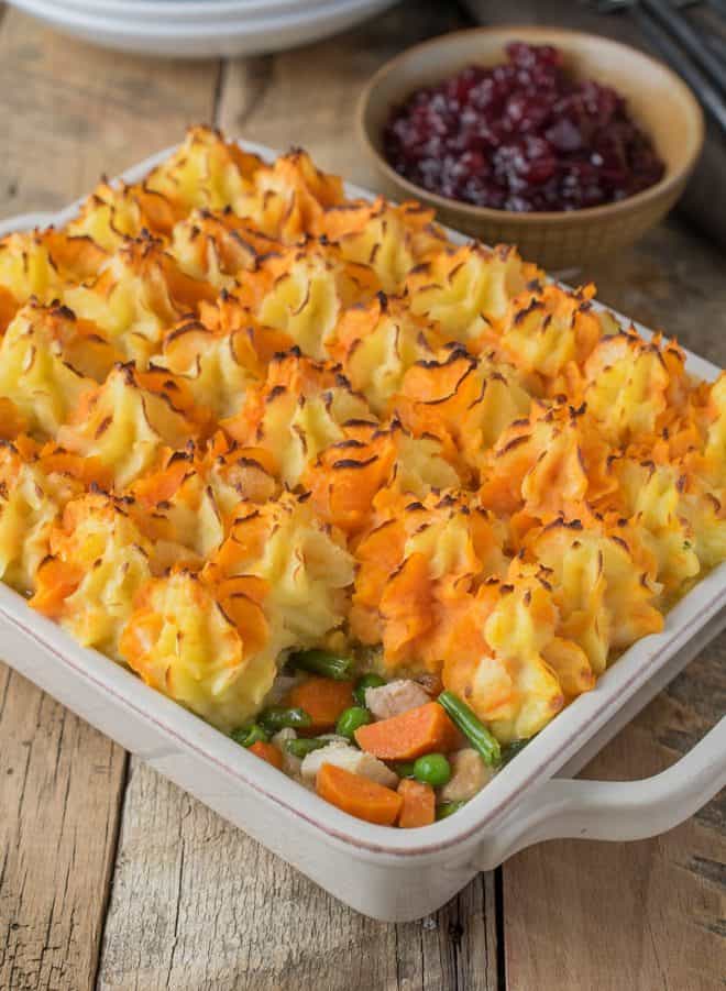 Orange and yellow mash topping leftover turkey and vegetables in a casserole dish with cranberry sauce