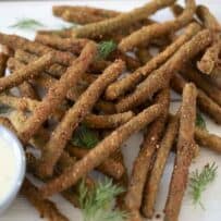 Long green beans that are fried, stacked on a board with a dipping sauce