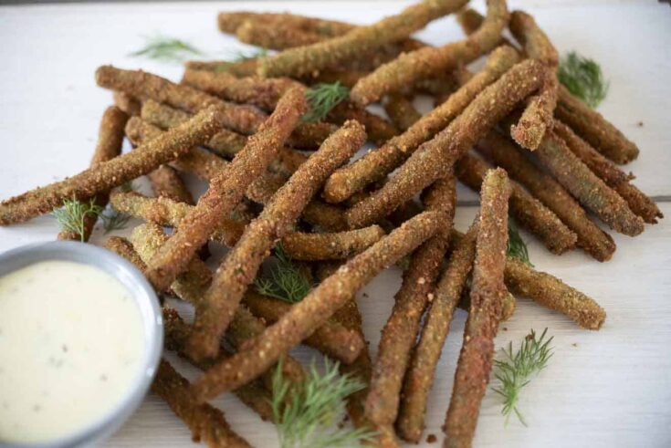 Long green beans that are fried, stacked on a board with a dipping sauce