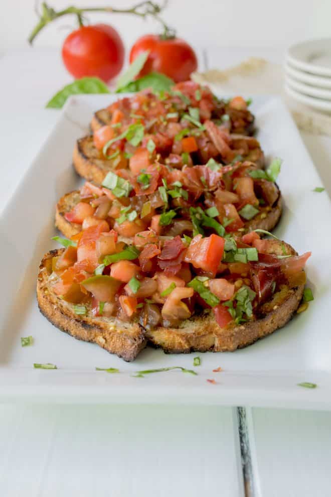 Crispy slices of bread topped with chopped tomato, basil and crispy prosciutto