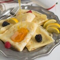 Thin pancakes on a plate served with syrup and fruit