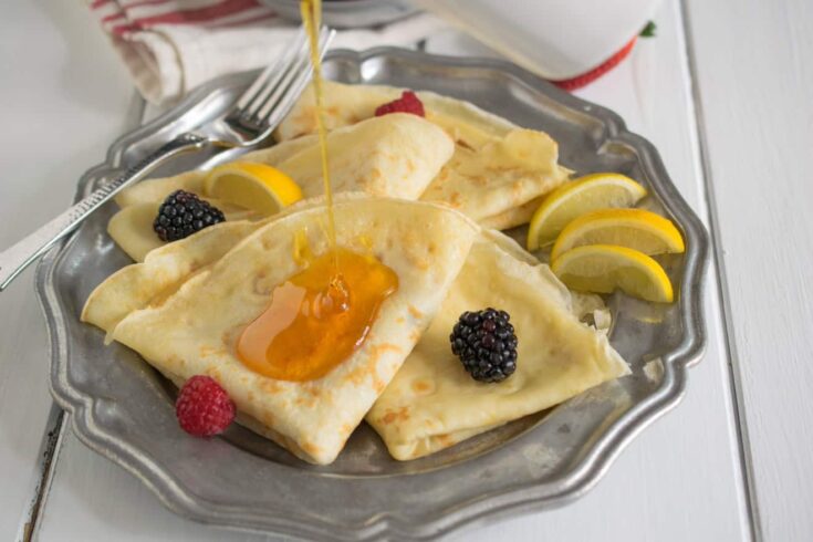 Thin pancakes on a plate served with syrup and fruit