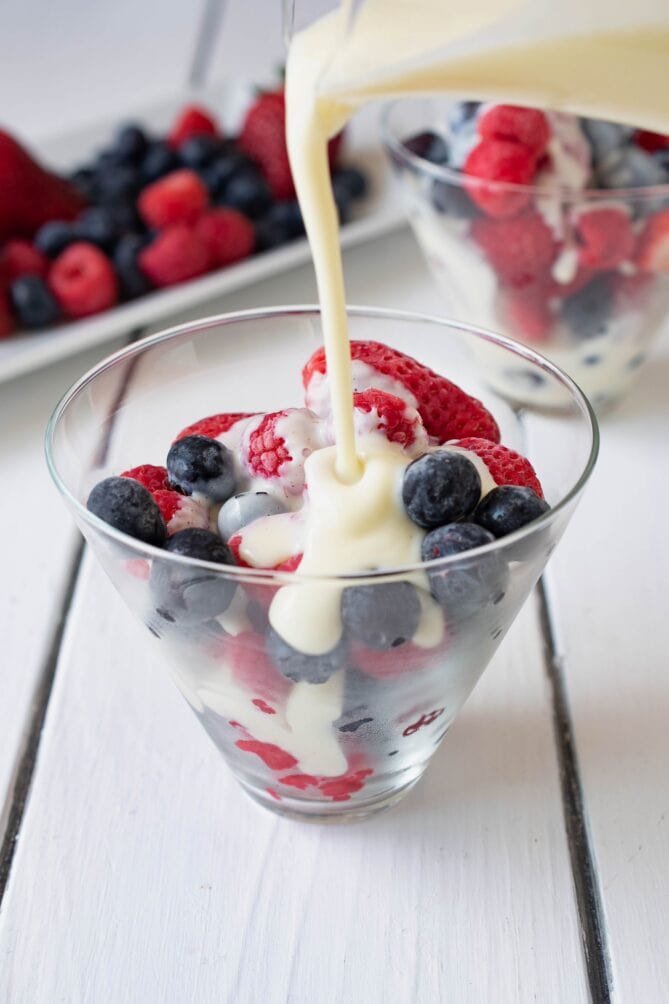 Pouring traditional English custard over mixed berries