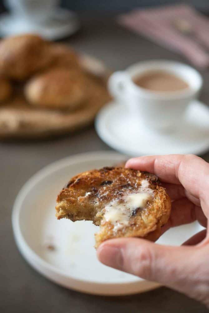 Holding half of a buttered teacake with a bite taken out